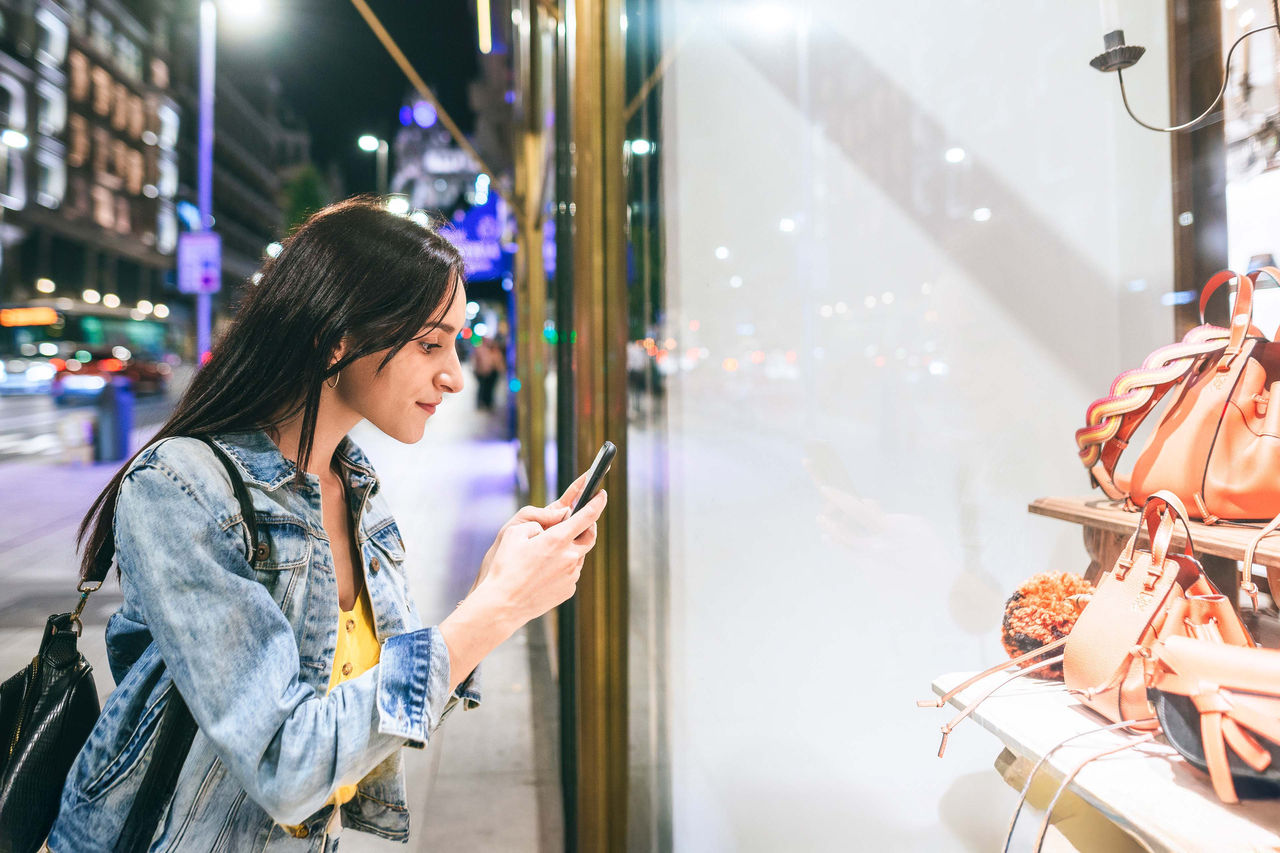 Woman taking a picture to shop window at night Woman taking a picture to shop window at night in Gran Via, Madrid