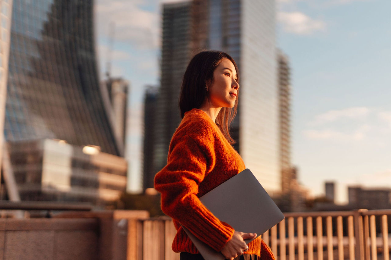 ey-studioplus-confident-young-asian-businesswoman-with-laptop-walking-in-the-city-against-skyscraper.jpeg