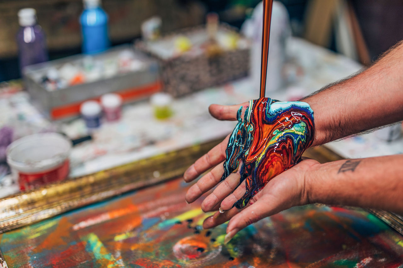 Male artist in his studio, pouring acrylic colors on canvas.