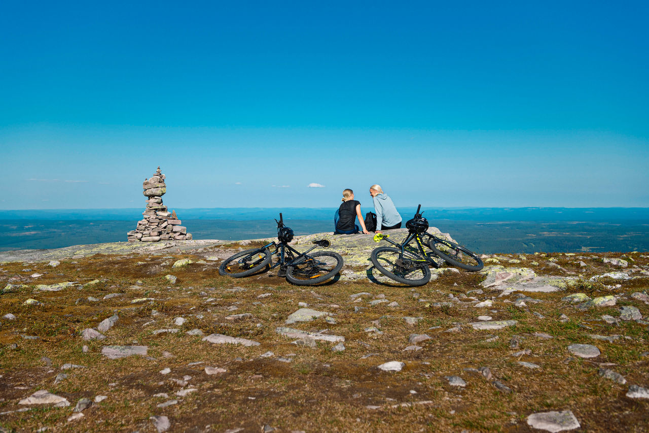 two women sit with their bikes on a hilltop in summer